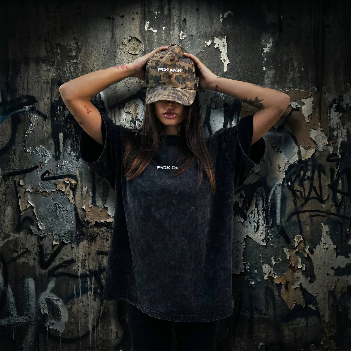 F*CK PAIN Distressed Camo Cap — female lifestyle hands on cap graffiti wall