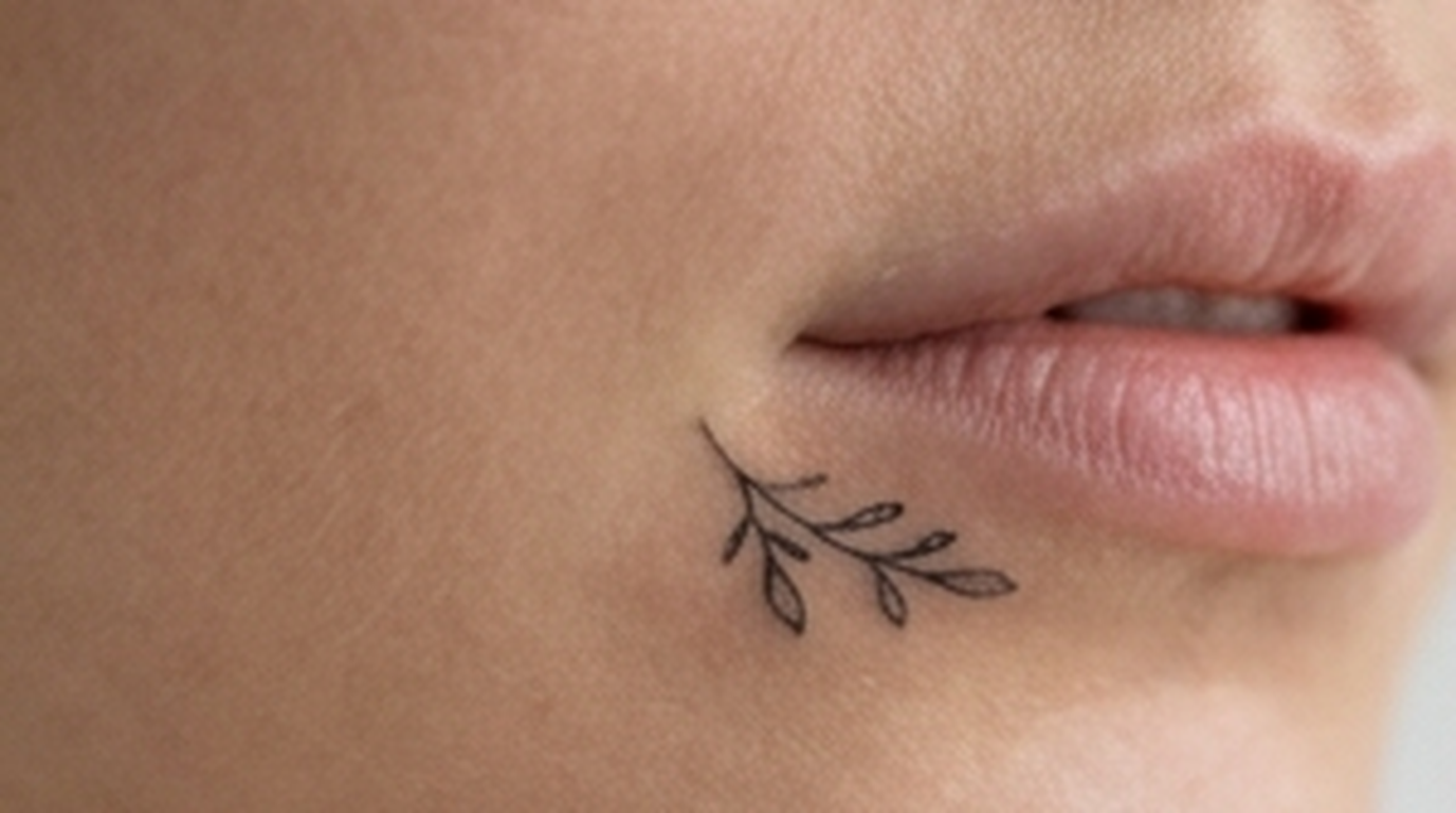 Delicate fine line botanical tattoo beside a person's lips