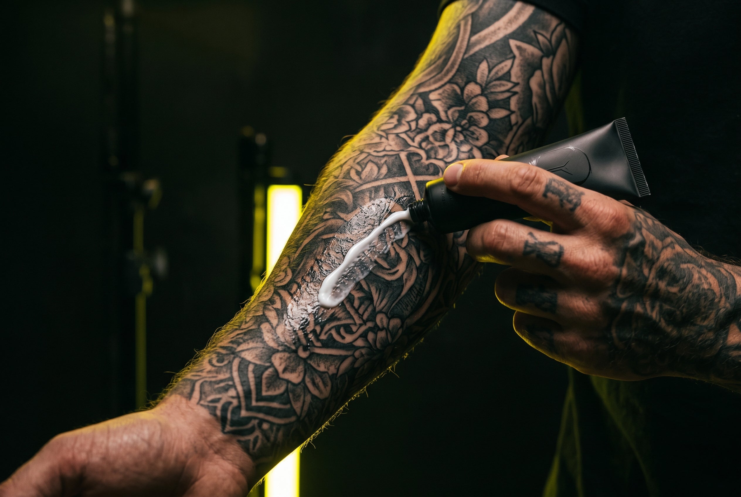 Tattoo numbing cream being applied to tattooed arm — dark studio aesthetic
