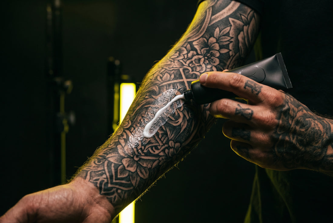 Tattoo numbing cream being applied to tattooed arm — dark studio aesthetic