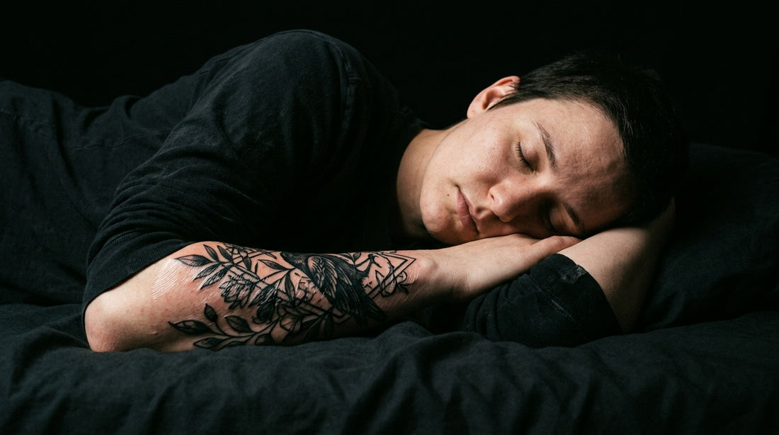 Person sleeping with tattooed arm visible — moody dark photography, tattoo healing guide